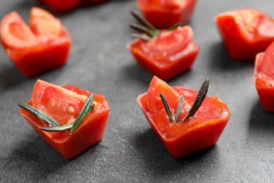 Photo of Ice cubes with tomatoes and rosemary on grey table, closeup