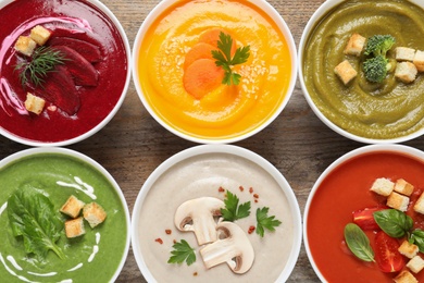 Various cream soups in bowls on wooden background, top view