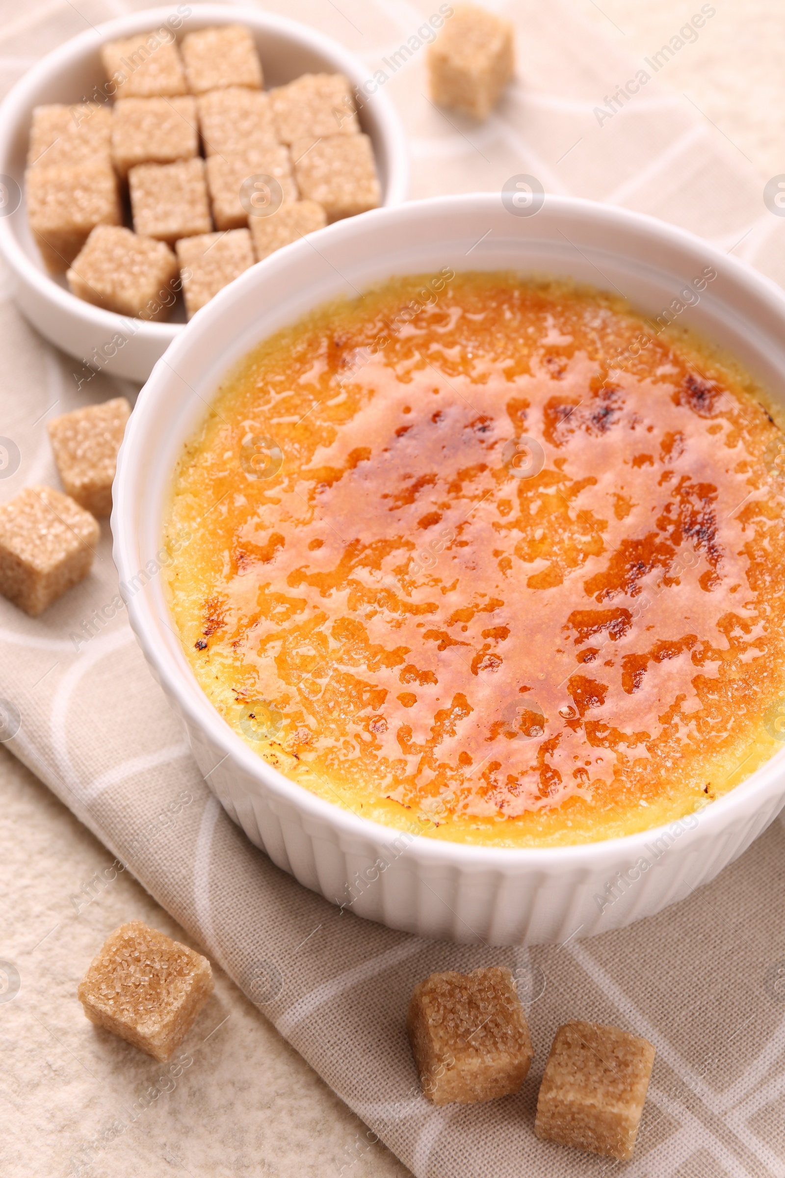 Photo of Delicious creme brulee in bowl and sugar cubes on light table, closeup