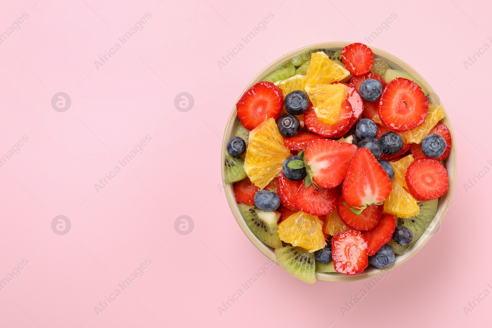 Photo of Yummy fruit salad in bowl on pink background, top view. Space for text