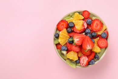 Photo of Yummy fruit salad in bowl on pink background, top view. Space for text