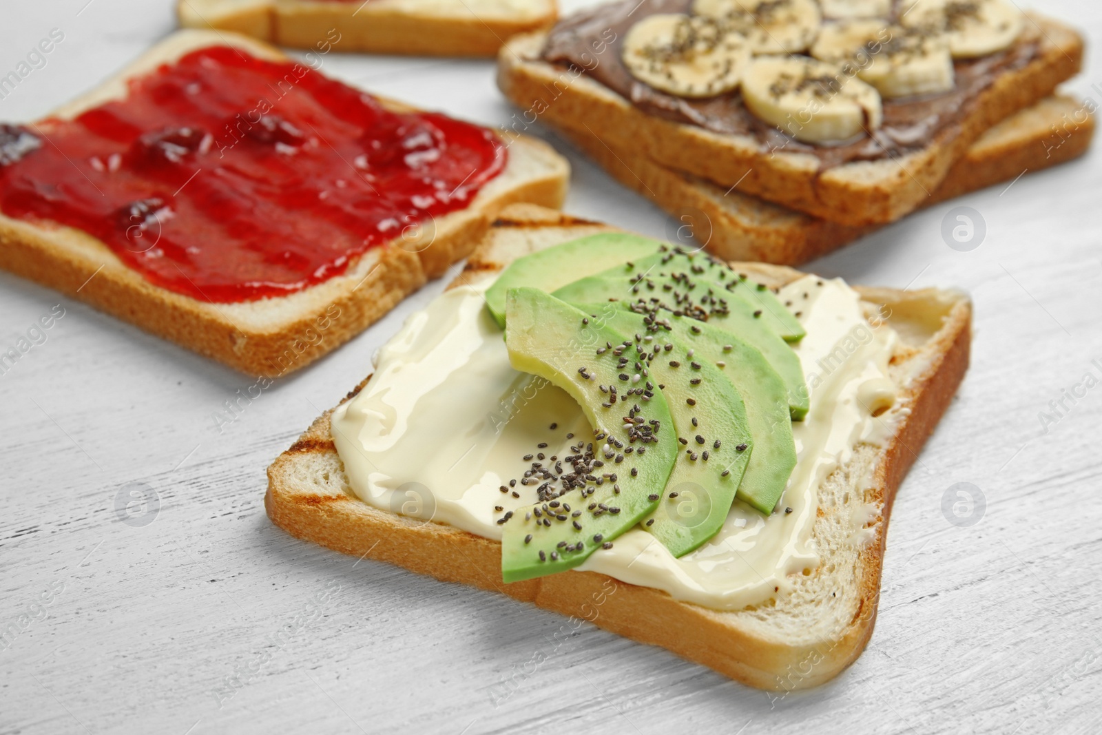 Photo of Slices of bread with different toppings on white wooden table