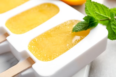 Photo of Tasty orange ice pops in mold on table, closeup. Fruit popsicle
