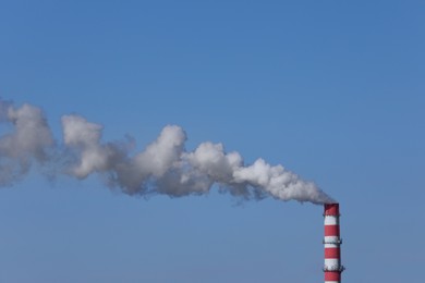 Polluting air with smoke from industrial chimney outdoors against blue sky. CO2 emissions