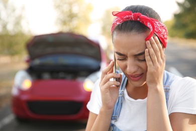 Photo of Stressed woman talking on phone near broken car outdoors