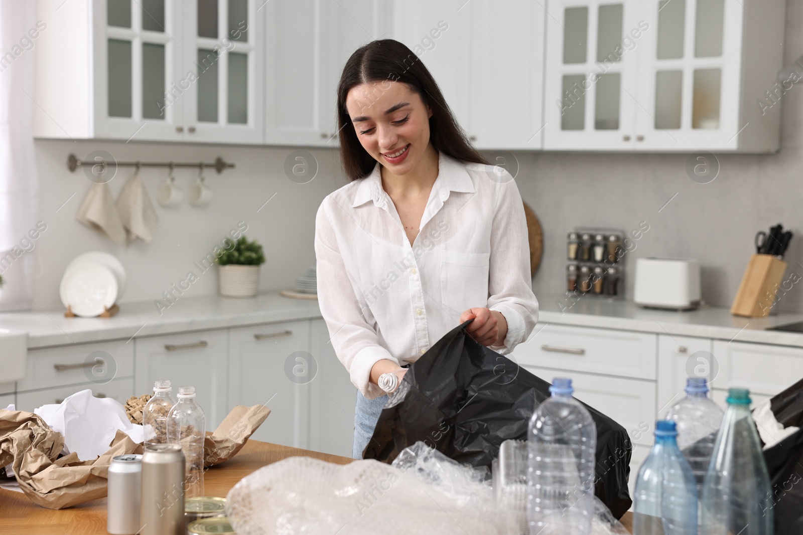 Photo of Smiling woman separating garbage at table in kitchen