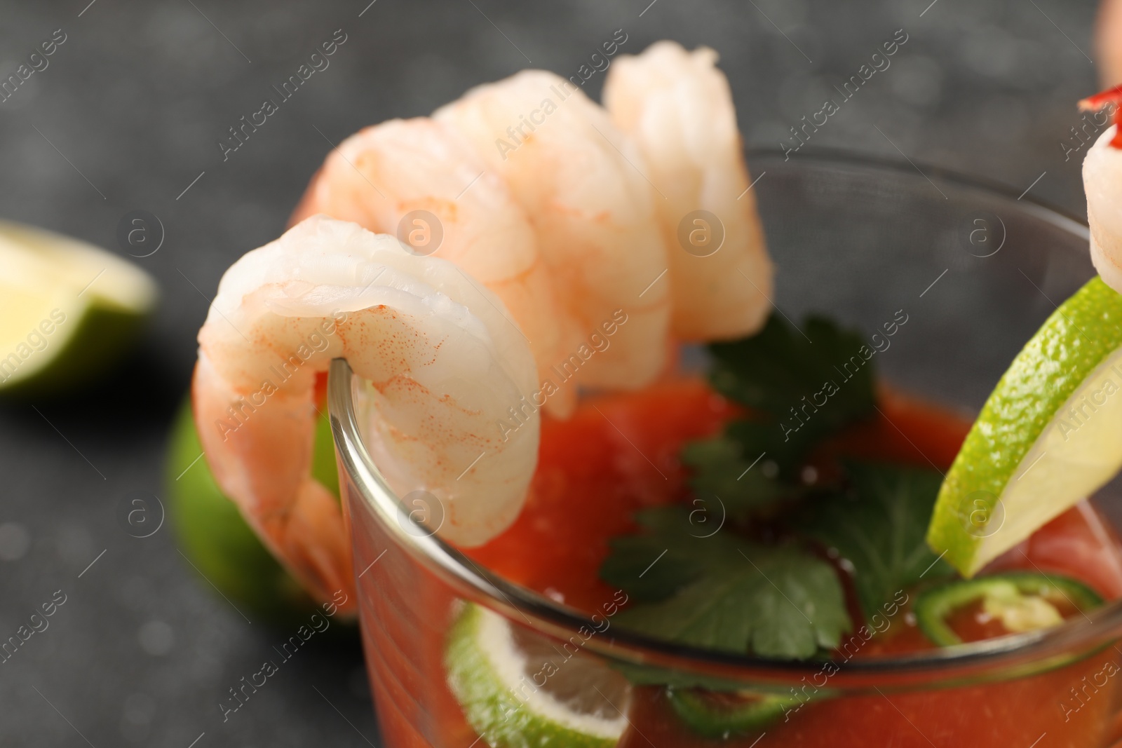 Photo of Tasty shrimp cocktail with sauce and lime in glass on grey table, closeup