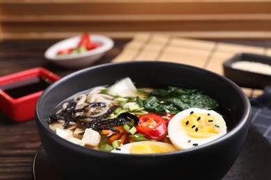 Delicious vegetarian ramen with egg, tofu and vegetables in bowl on table, closeup. Noodle soup