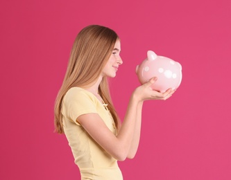 Teen girl with piggy bank on color background