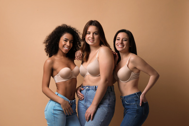 Group of women with different body types in jeans and underwear on beige background