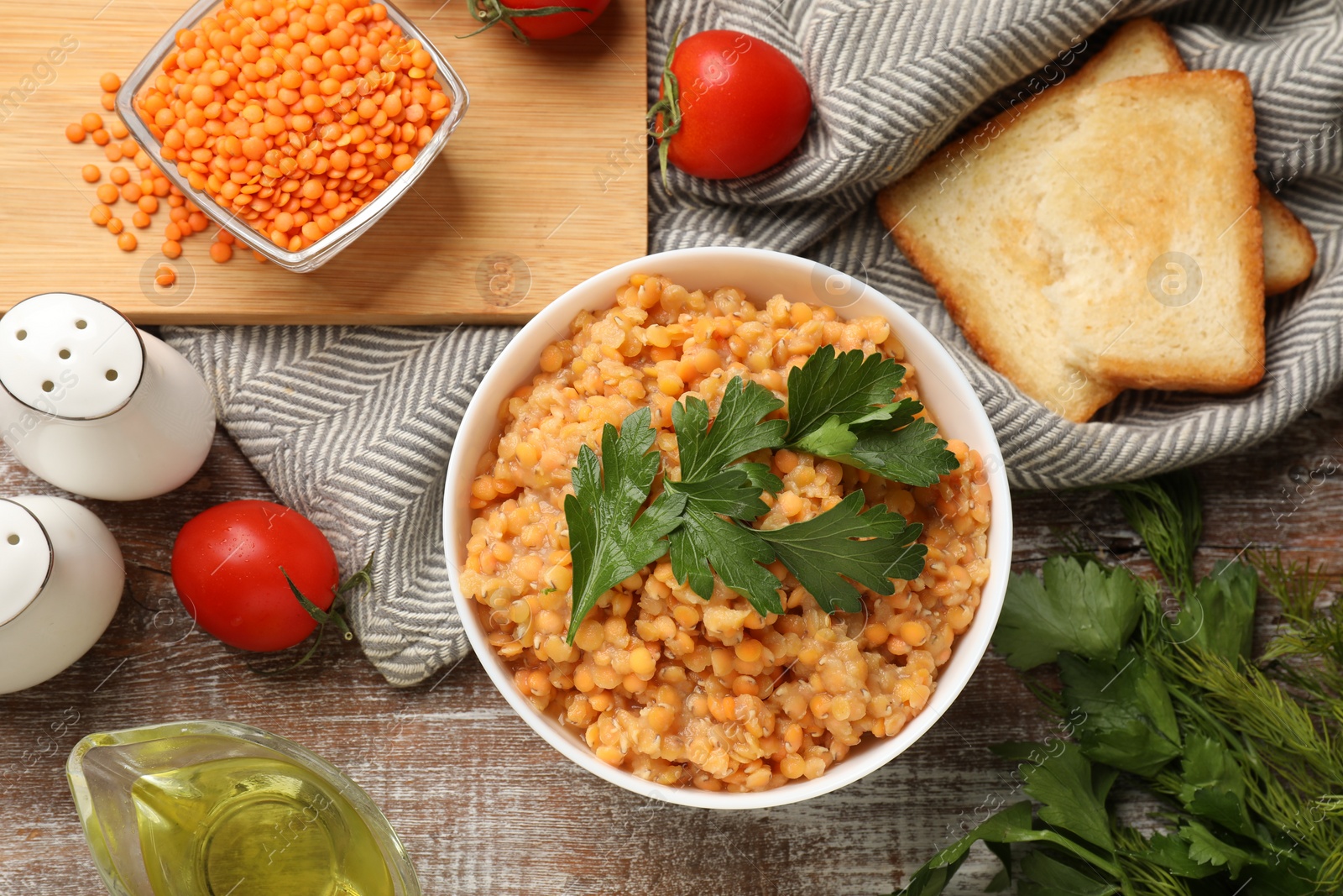 Photo of Delicious red lentils with parsley, tomatoes and bread on wooden table, flat lay