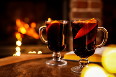 Photo of Tasty mulled wine, festive lights and blurred fireplace on background