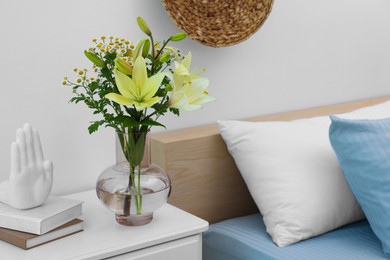Vase with bouquet of fresh flowers on nightstand in bedroom