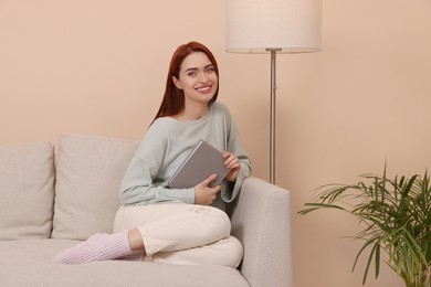 Photo of Happy woman with red dyed hair and book sitting on sofa indoors