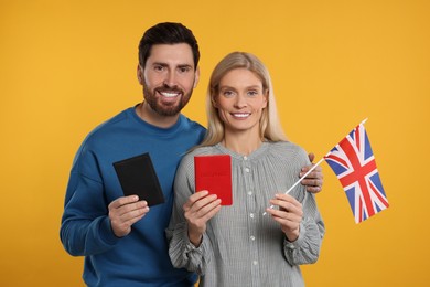 Immigration. Happy couple with passports and flag of United Kingdom on orange background