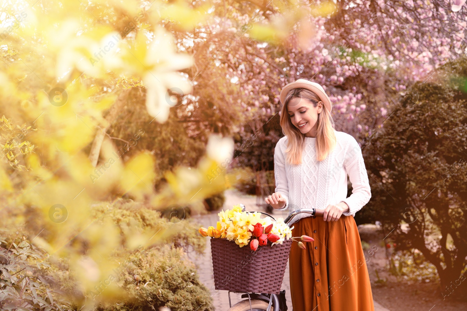 Image of Beautiful young woman with bicycle and flowers in park on sunny day