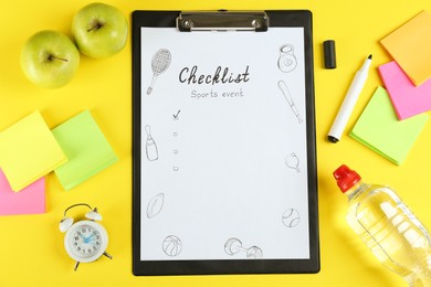 Photo of Sports Event Checklist. Flat lay composition with clipboard, alarm clock and bottle of water on yellow background
