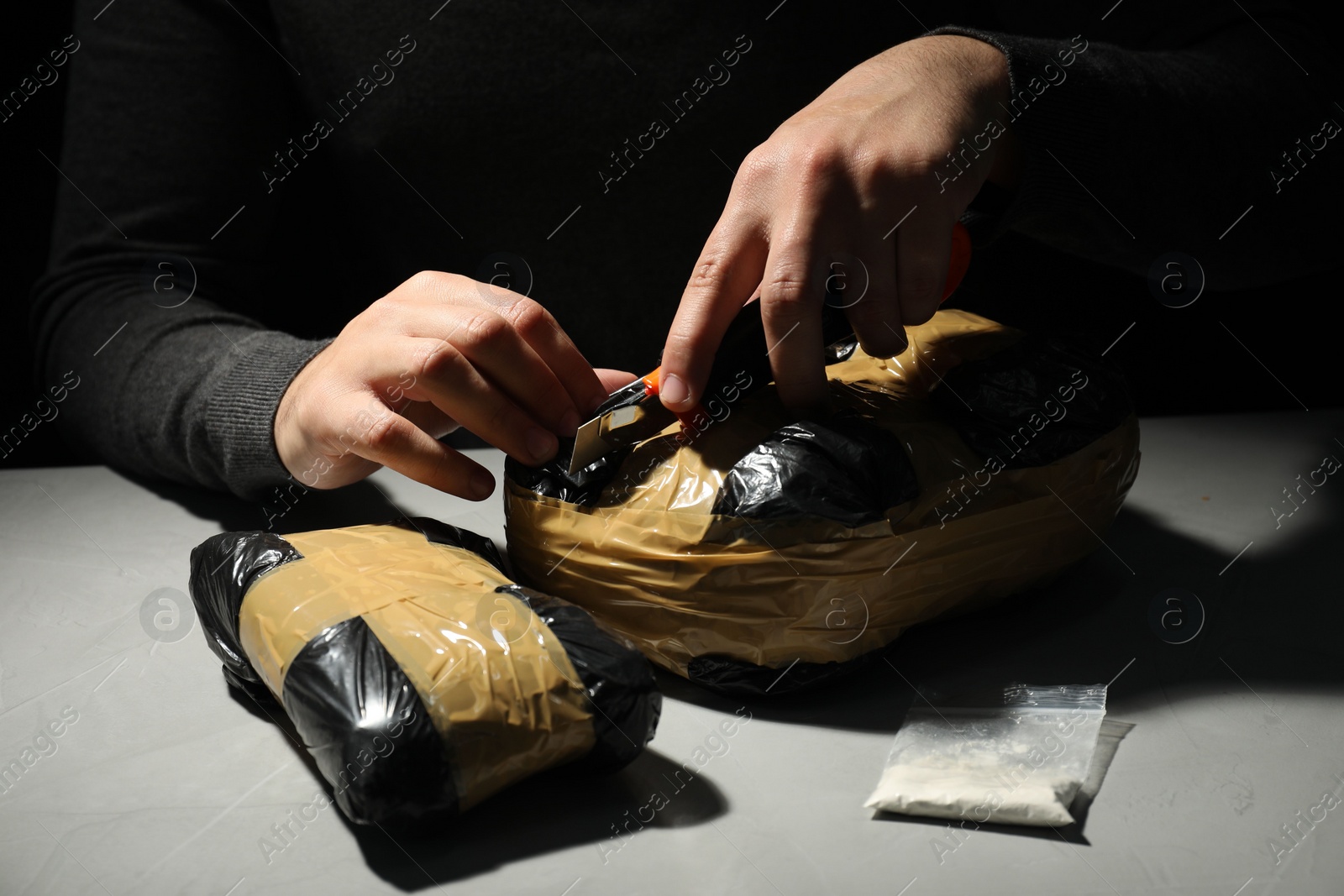 Photo of Smuggling and drug trafficking. Man opening package of narcotics with box cutter in darkness, closeup