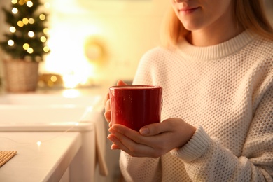 Photo of Woman holding cup with hot drink in kitchen, closeup