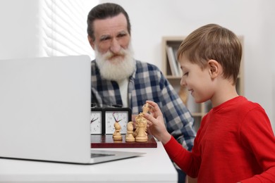 Grandfather and grandson playing chess following online lesson in room