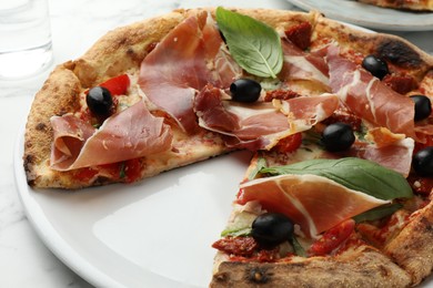 Photo of Tasty pizza with cured ham, olives, sun-dried tomato and basil on table, closeup