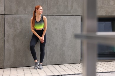 Photo of Beautiful woman in stylish gym clothes posing near grey wall on street
