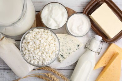 Different fresh dairy products and wheat ears on white wooden table, flat lay