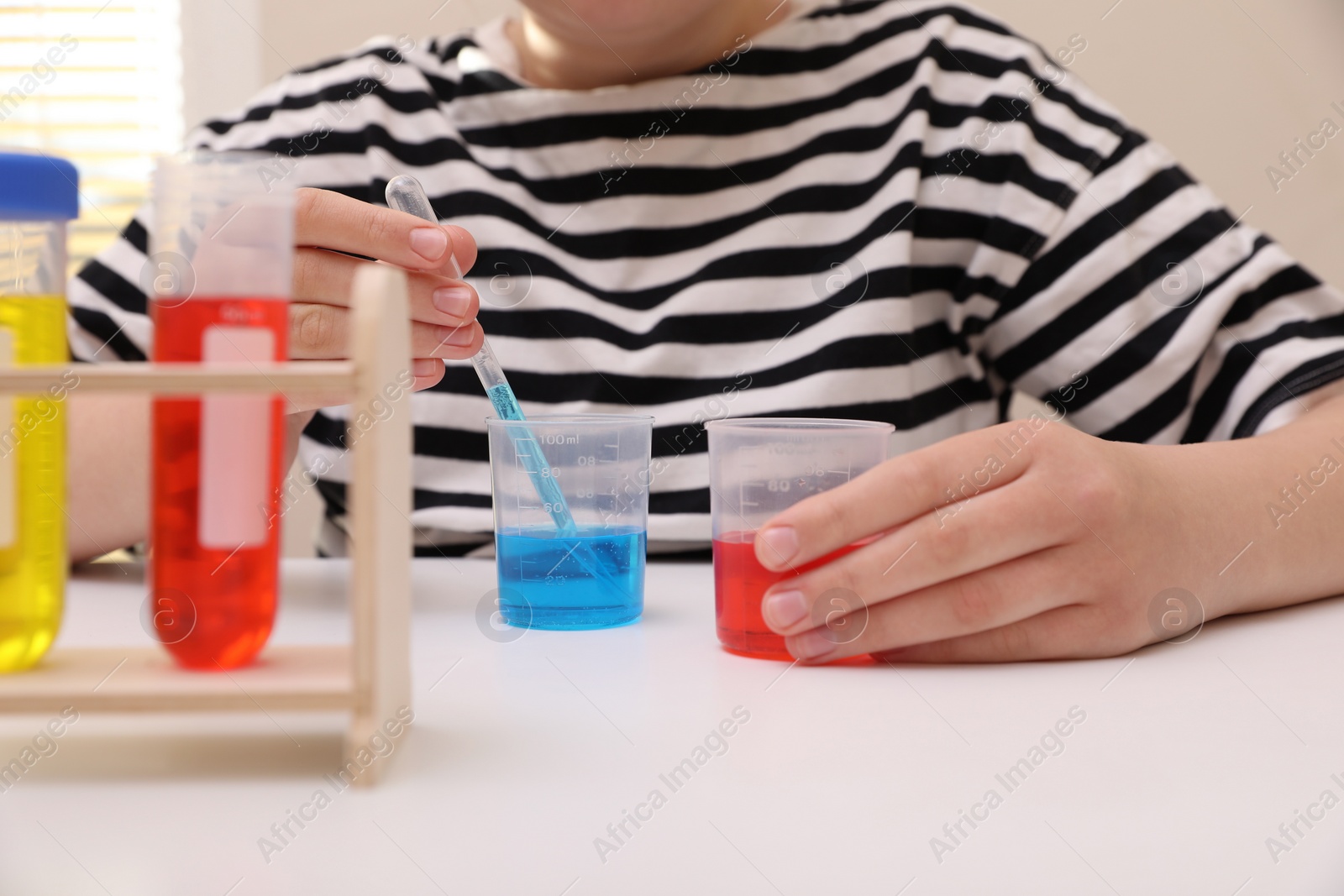 Photo of Girl mixing colorful liquids at white table indoors, closeup. Chemical experiment set for kids