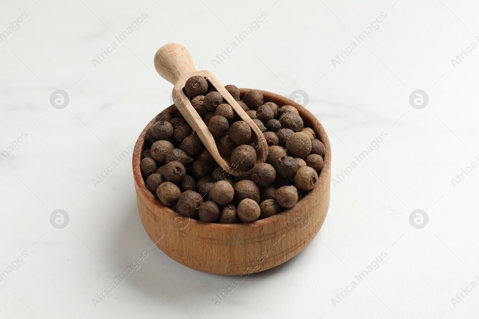 Photo of Dry allspice berries (Jamaica pepper) in bowl and scoop on white marble table