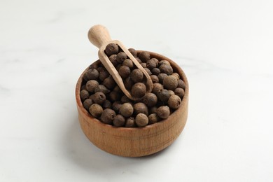 Dry allspice berries (Jamaica pepper) in bowl and scoop on white marble table