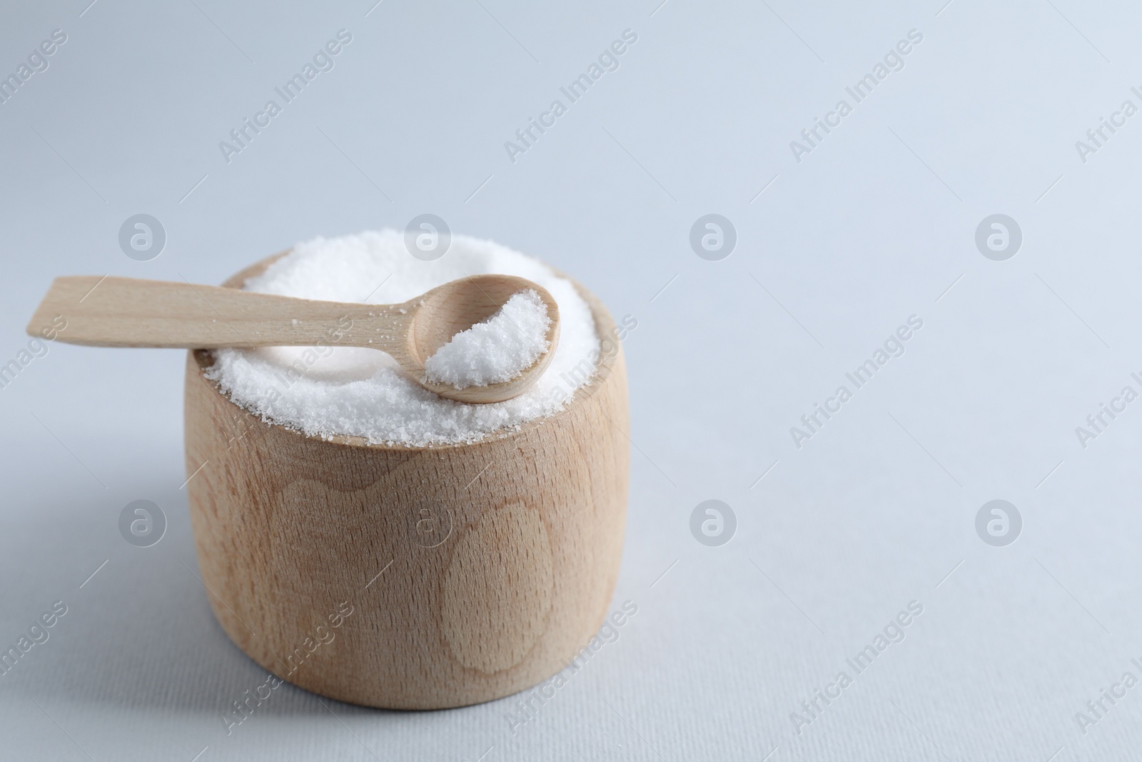 Photo of Organic white salt in bowl and spoon on light grey background, closeup. Space for text