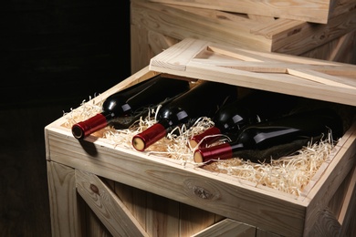 Wooden crate with bottles of wine on dark background, closeup