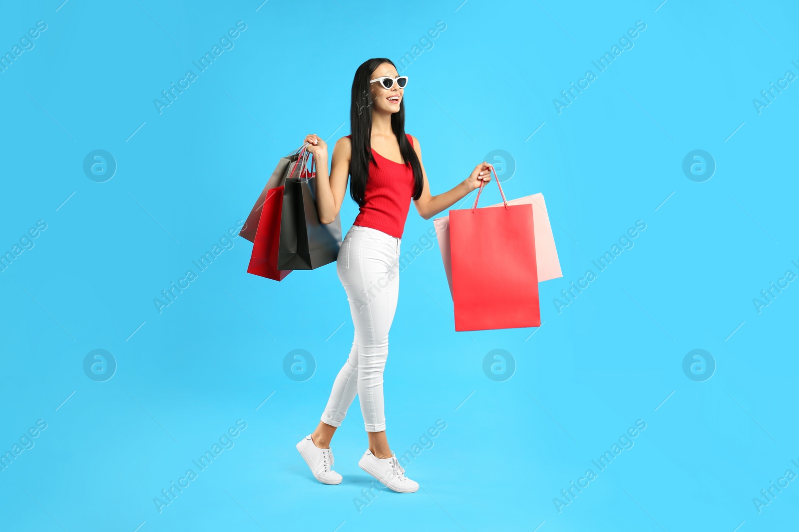 Photo of Beautiful young woman with paper shopping bags on light blue background