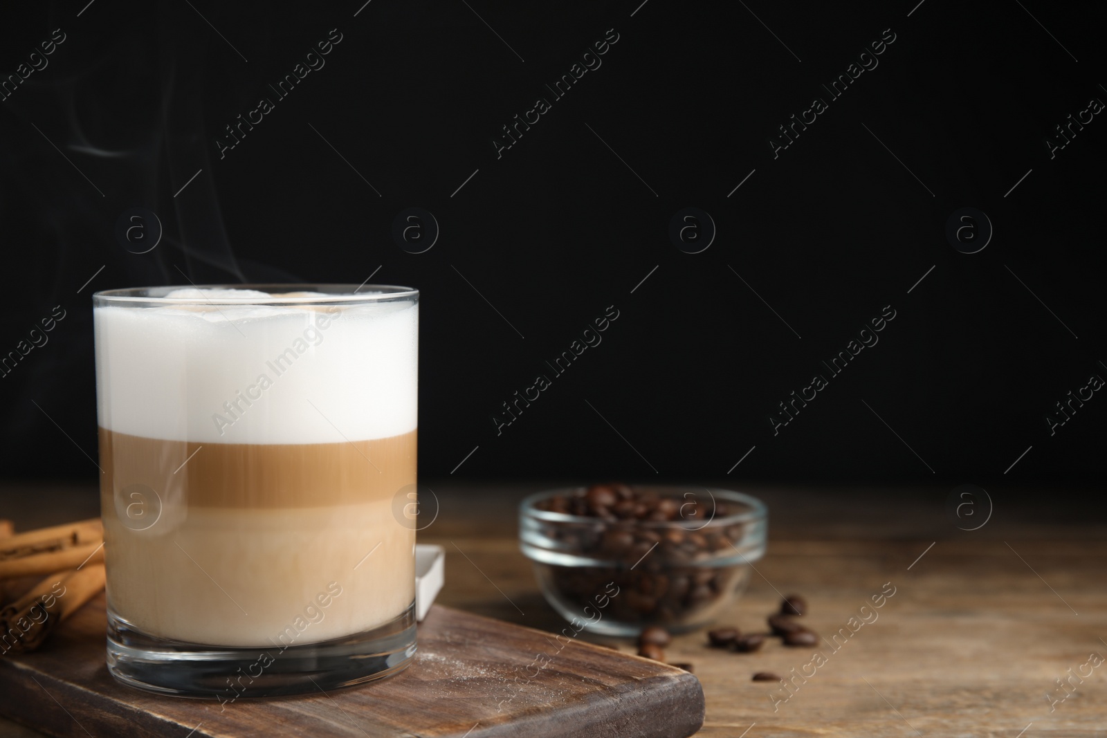 Photo of Delicious latte macchiato, cinnamon sticks and coffee beans on wooden table, space for text