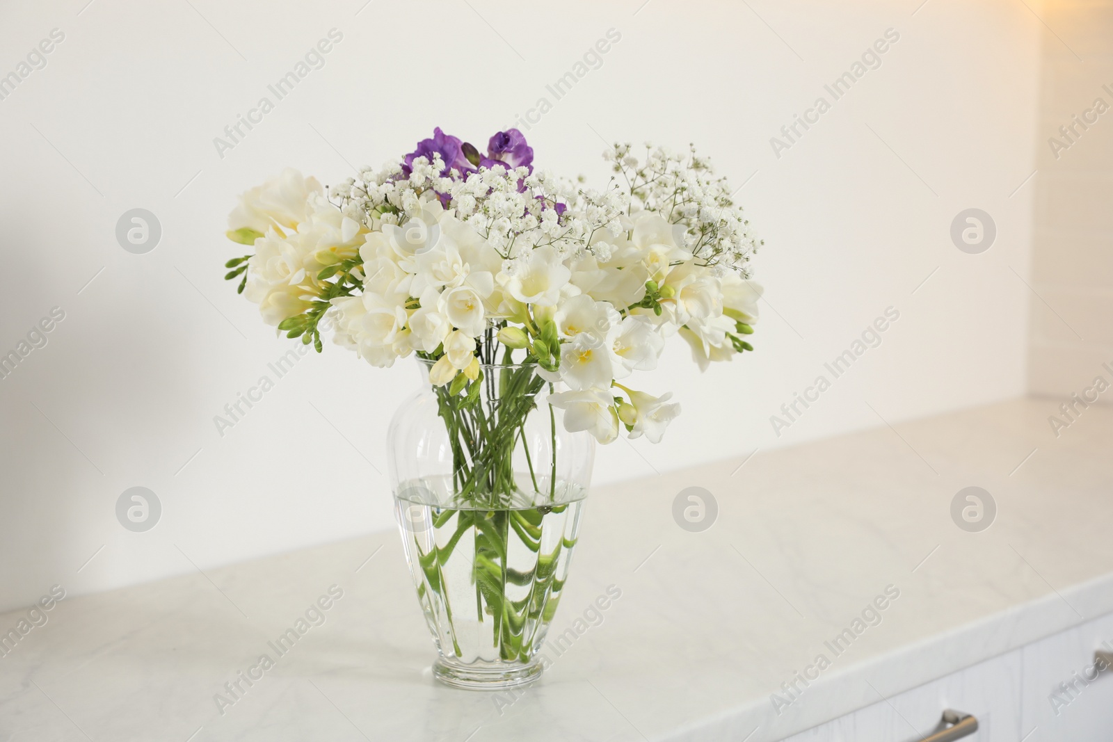 Photo of Beautiful bouquet with fresh freesia flowers in vase on cabinet indoors