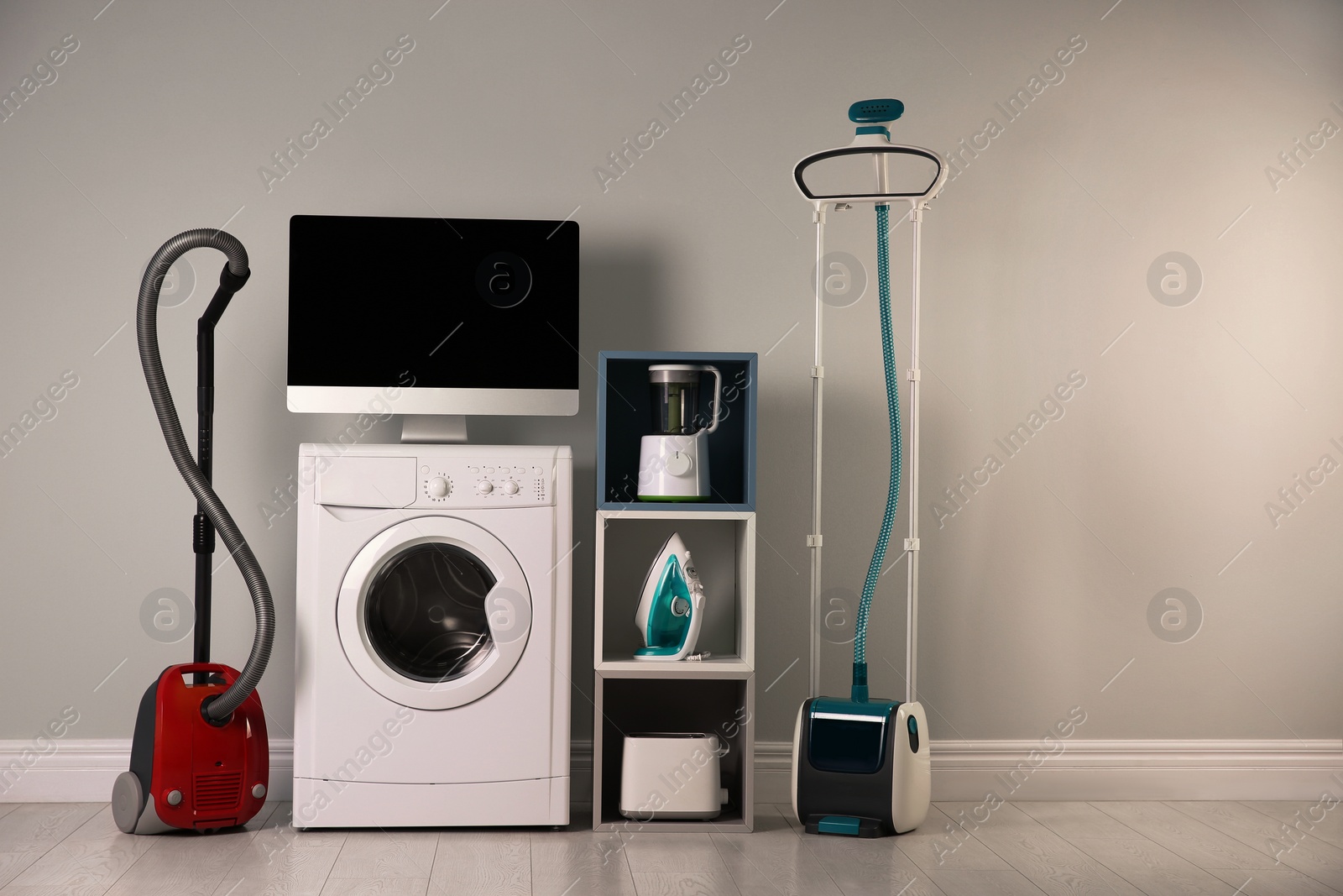 Photo of Modern vacuum cleaner and different household appliances near light wall indoors