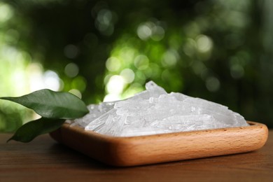 Photo of Menthol crystals and green leaves on wooden table against blurred background, closeup