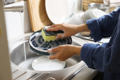 Photo of Woman washing plate in kitchen sink, closeup