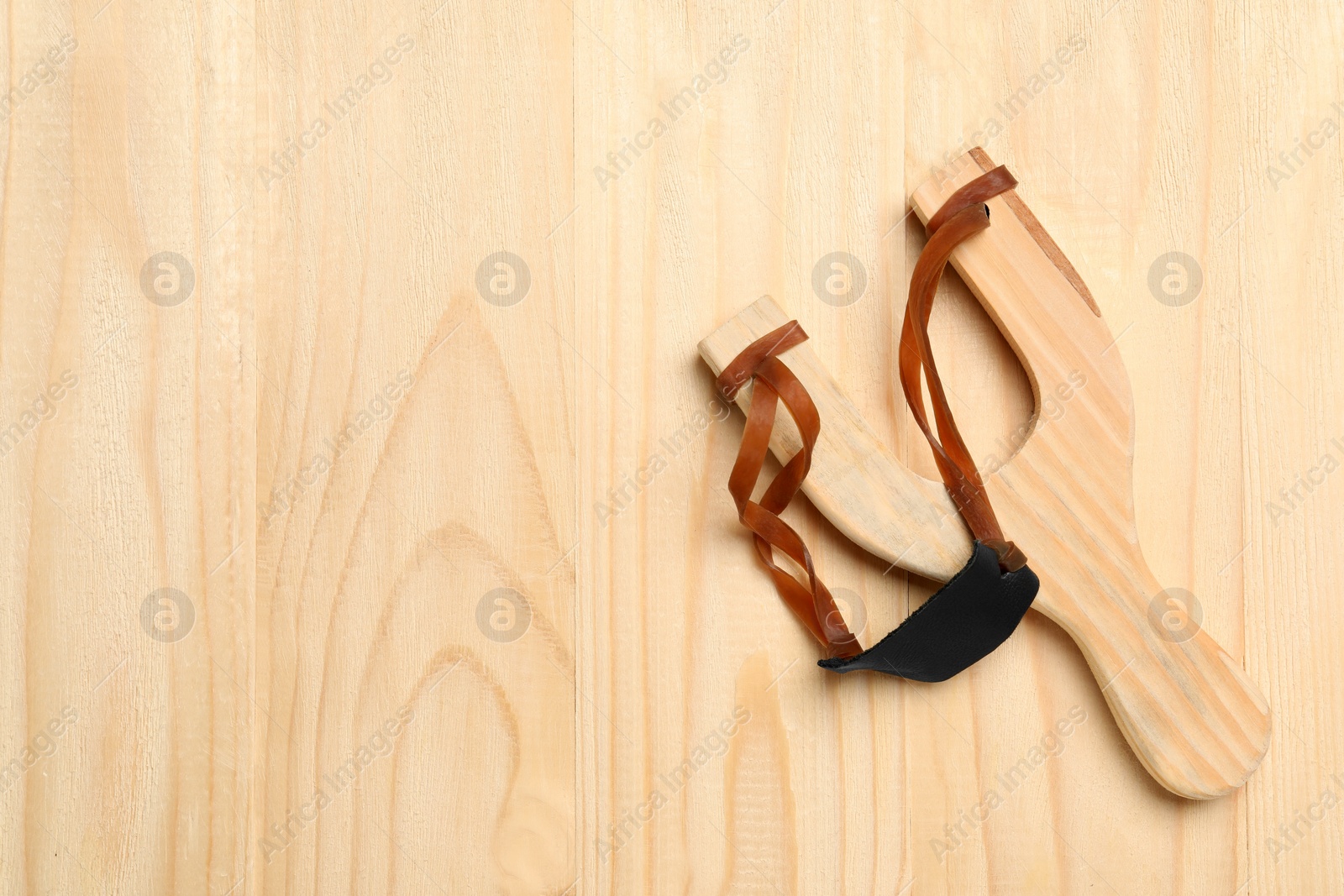 Photo of Slingshot with leather pouch on wooden background, top view. Space for text