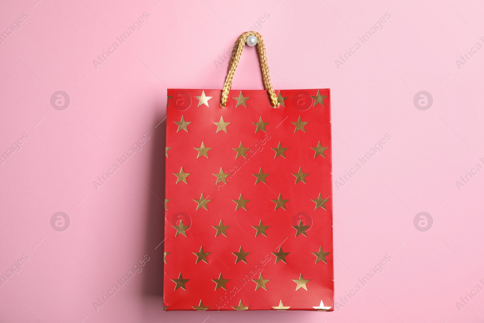 Photo of Red shopping paper bag with star pattern on pink background