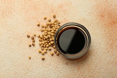 Photo of Soy sauce in bowl and beans on beige textured table, flat lay