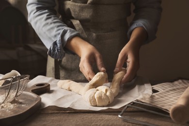 Woman making braided bread at wooden table, closeup. Traditional Shabbat challah