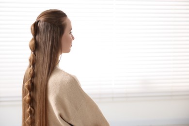 Photo of Young woman with long braided hair indoors, space for text