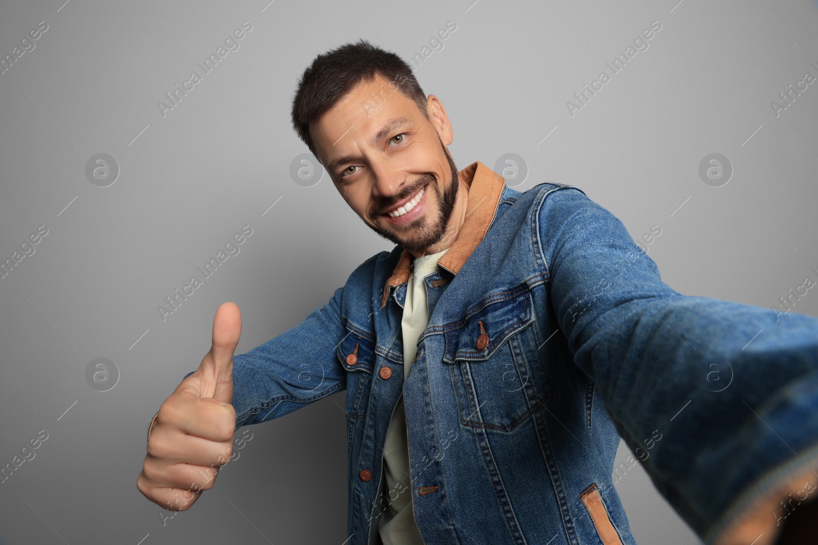 Photo of Man showing thumb up while taking selfie on grey background