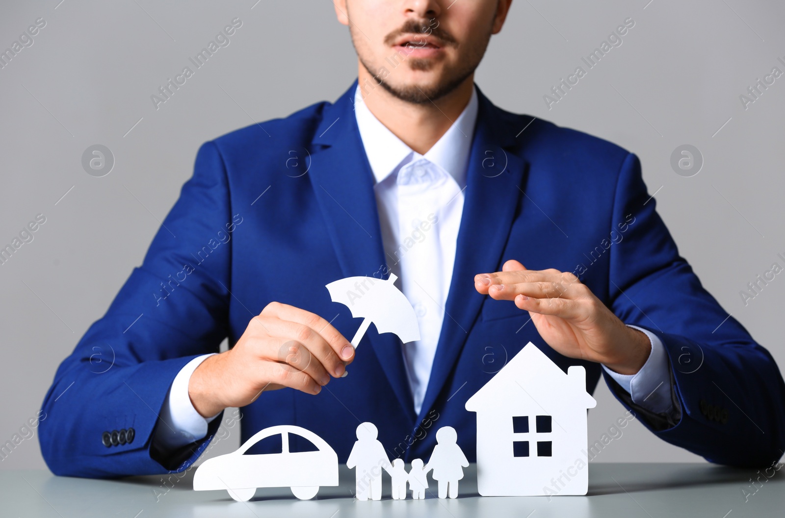 Photo of Male insurance agent covering paper family, car and home with umbrella cutout at table, closeup