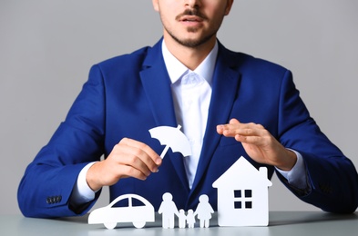 Male insurance agent covering paper family, car and home with umbrella cutout at table, closeup