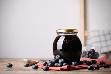 Jar of blueberry jam and fresh berries on wooden table. Space for text