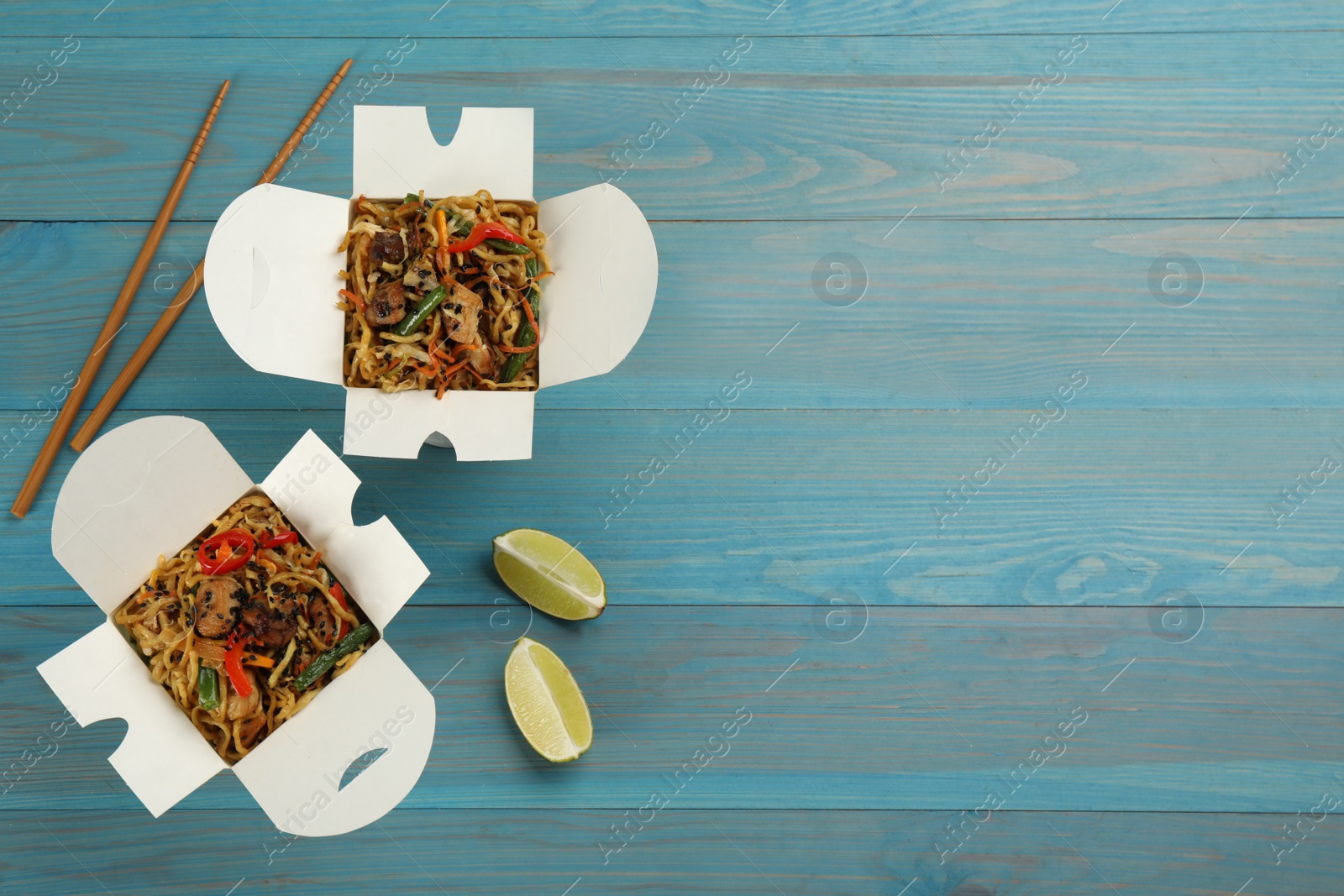 Photo of Boxes of wok noodles with vegetables, meat and chopsticks on light blue wooden table, flat lay. Space for text