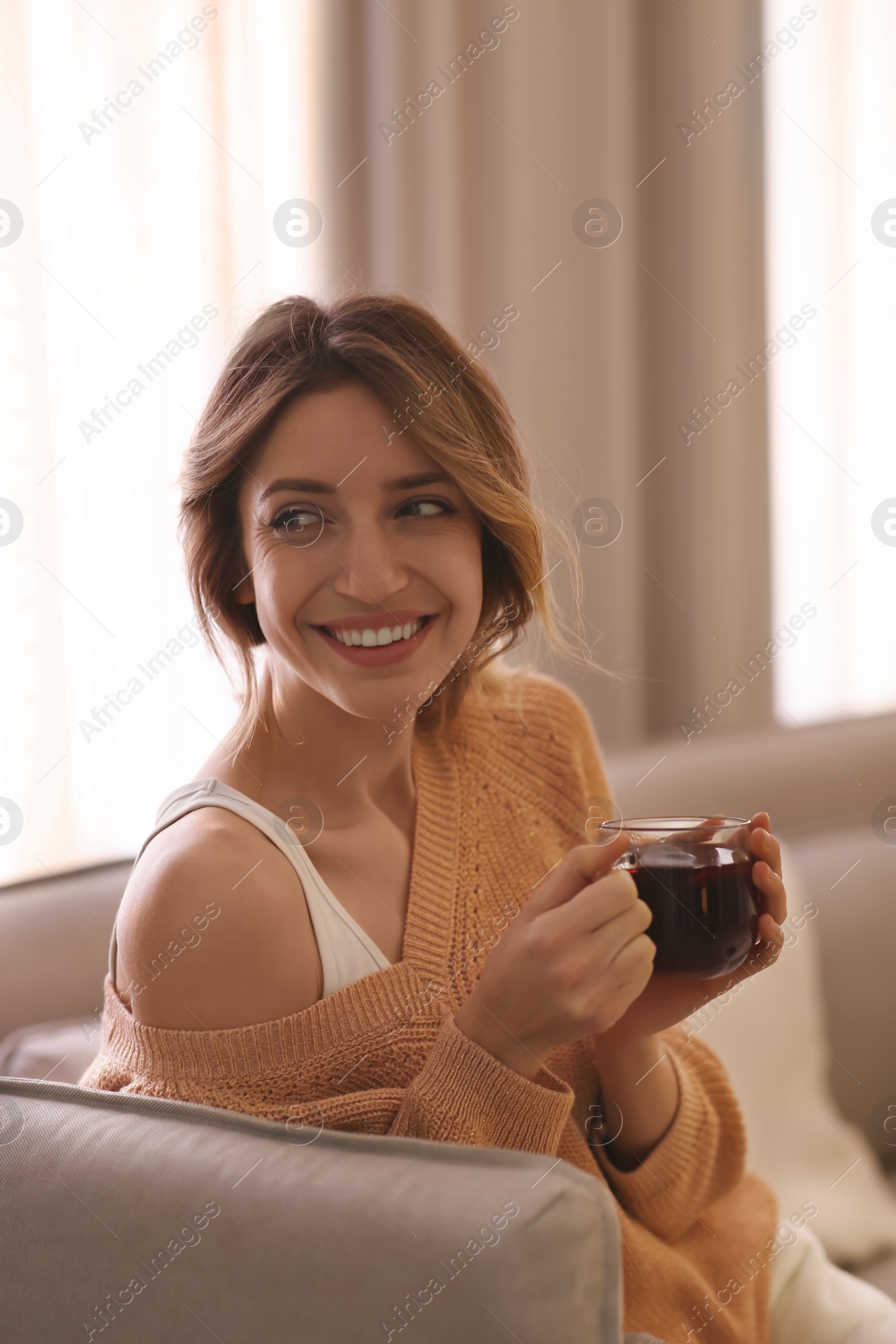 Photo of Beautiful young woman with cup of tea relaxing at home. Cozy atmosphere