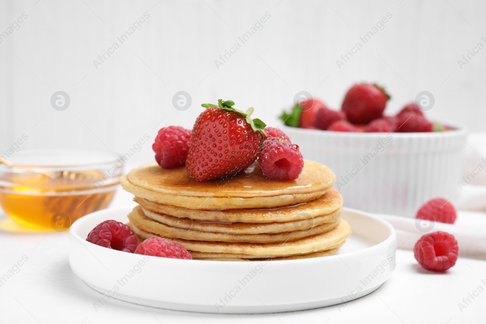 Photo of Tasty pancakes with fresh berries and honey on white table